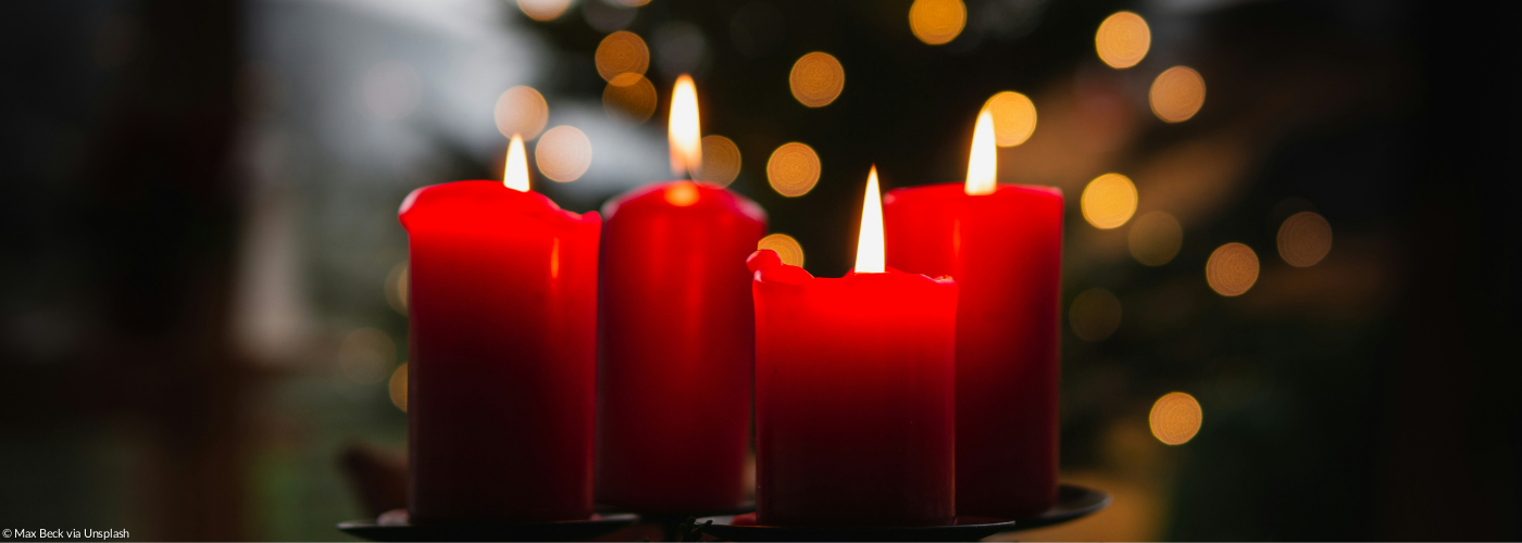 Vier rote brennende Adventskerzen vor einem leuchtenden Christbaum