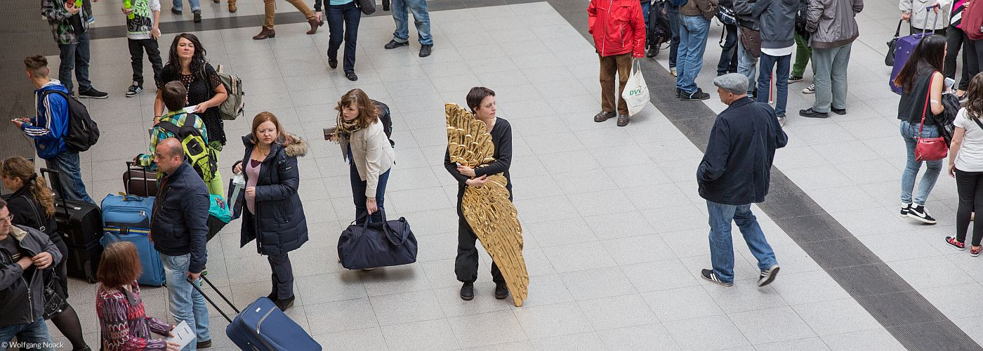 Ein Engel steht in der Bahnhofshalle inmitten von Reisenden