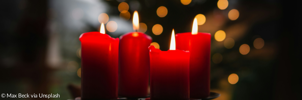 Vier rote brennende Adventskerzen vor einem leuchtenden Christbaum
