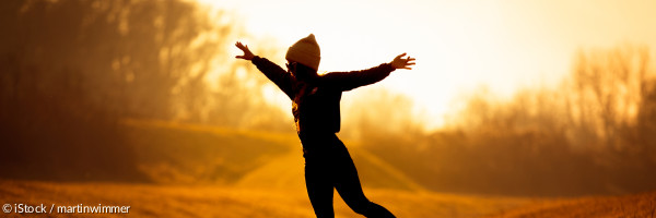 Eine junge Frau balanciert auf einem schmalen Steg über einem Bach im Herbstlicht