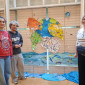 Drei Mitarbeiter:innen beim Osterferienworkshop für Kinder stehen vor einem Bühnenbild mit Meer